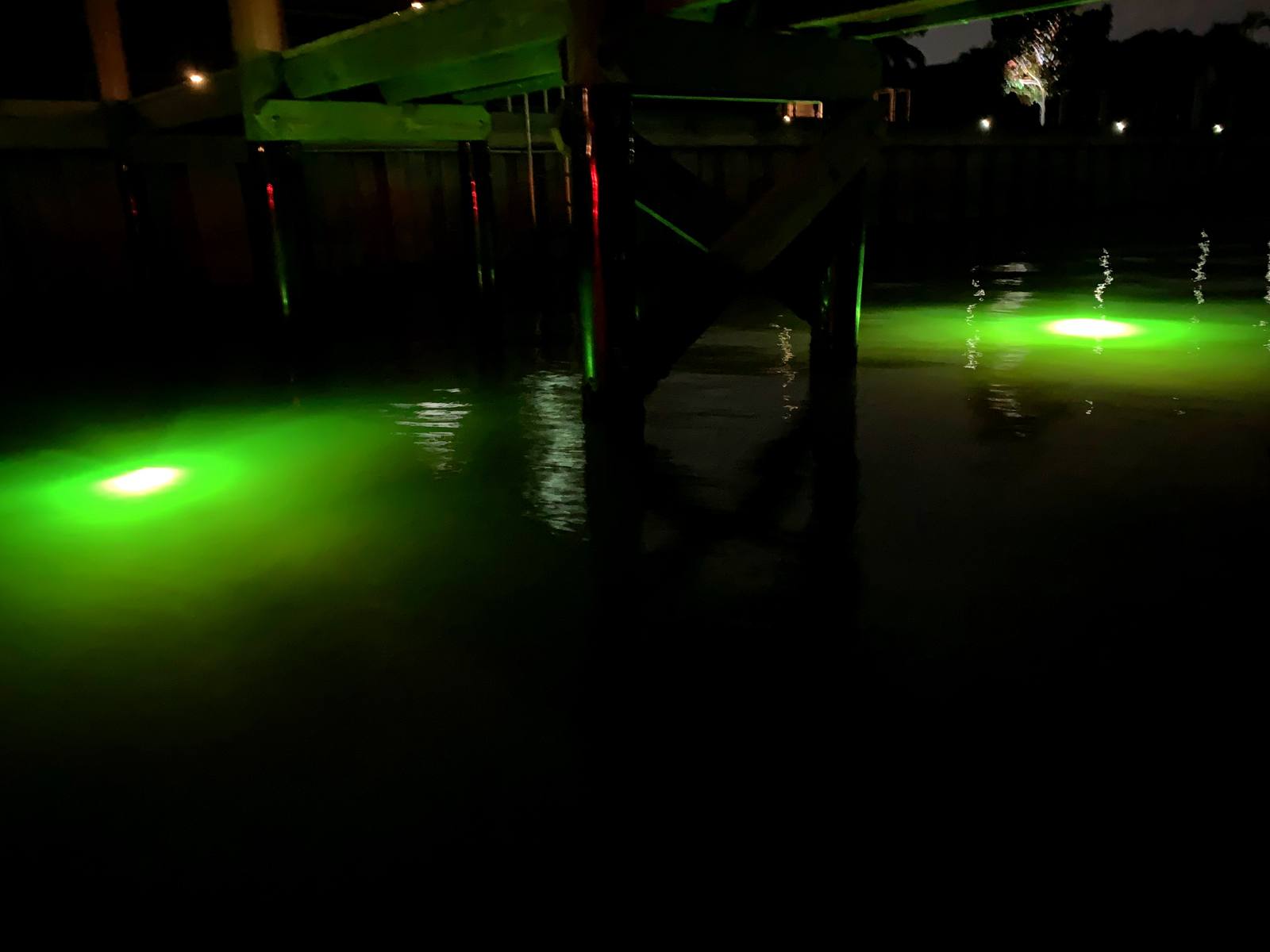 Submerged dock lights glowing green on the water at night