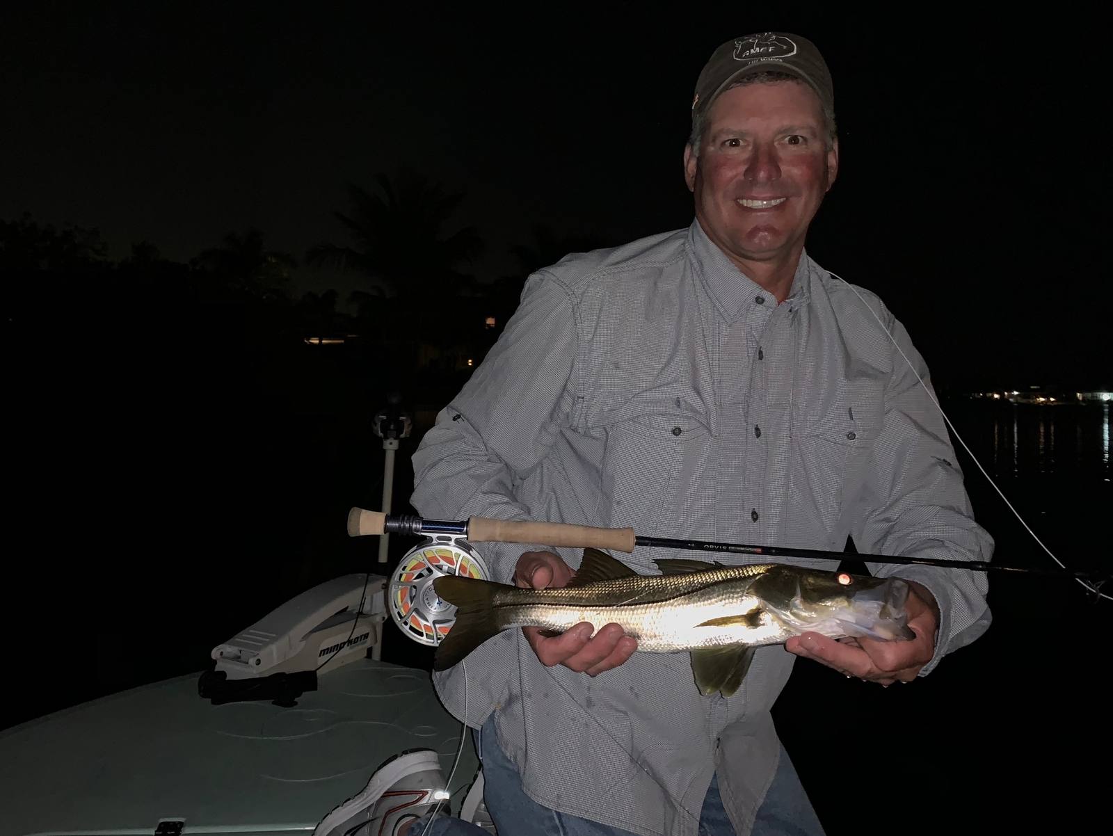 A happy angler holding a snook caught on the dock lights at night