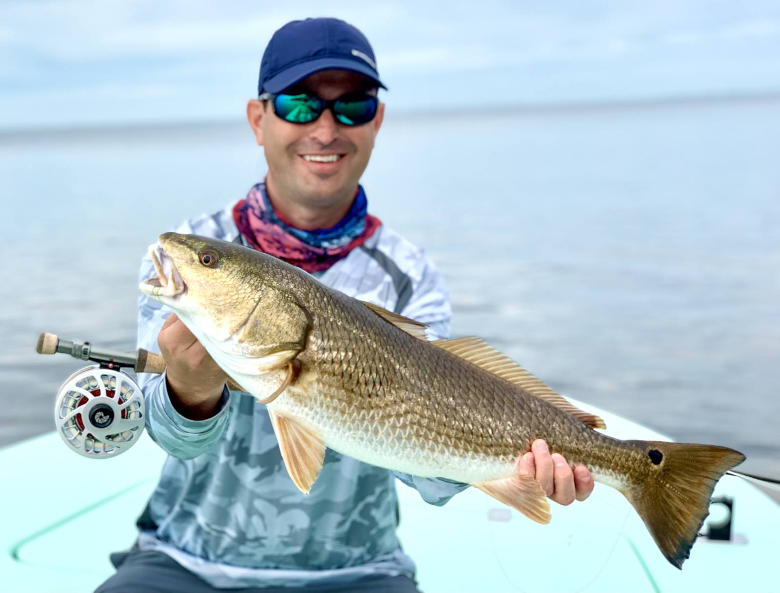 Angler holding a redfish with a fly rod tucked under his arm