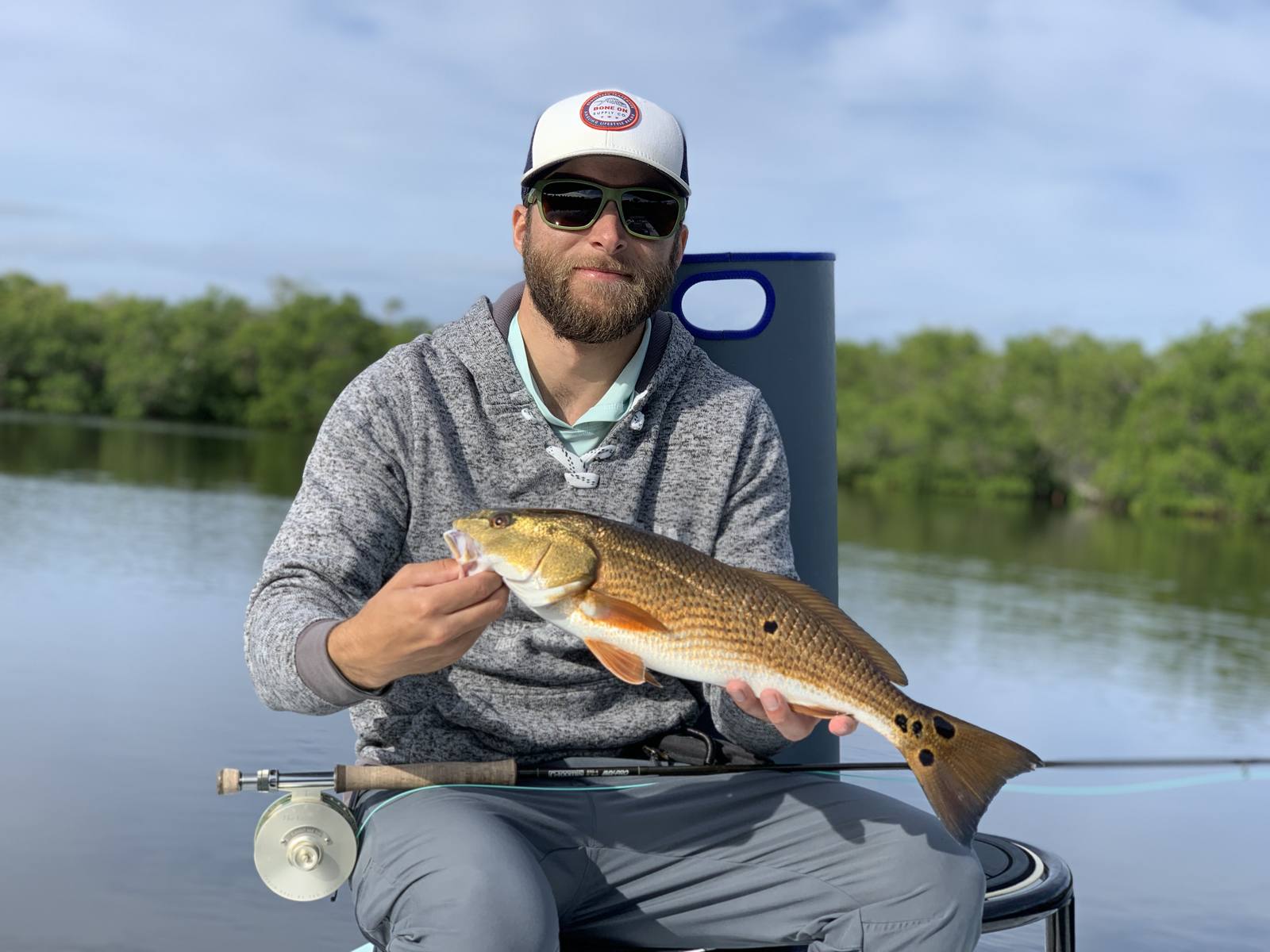 Seated angler admiring a redfish beside the mangroves