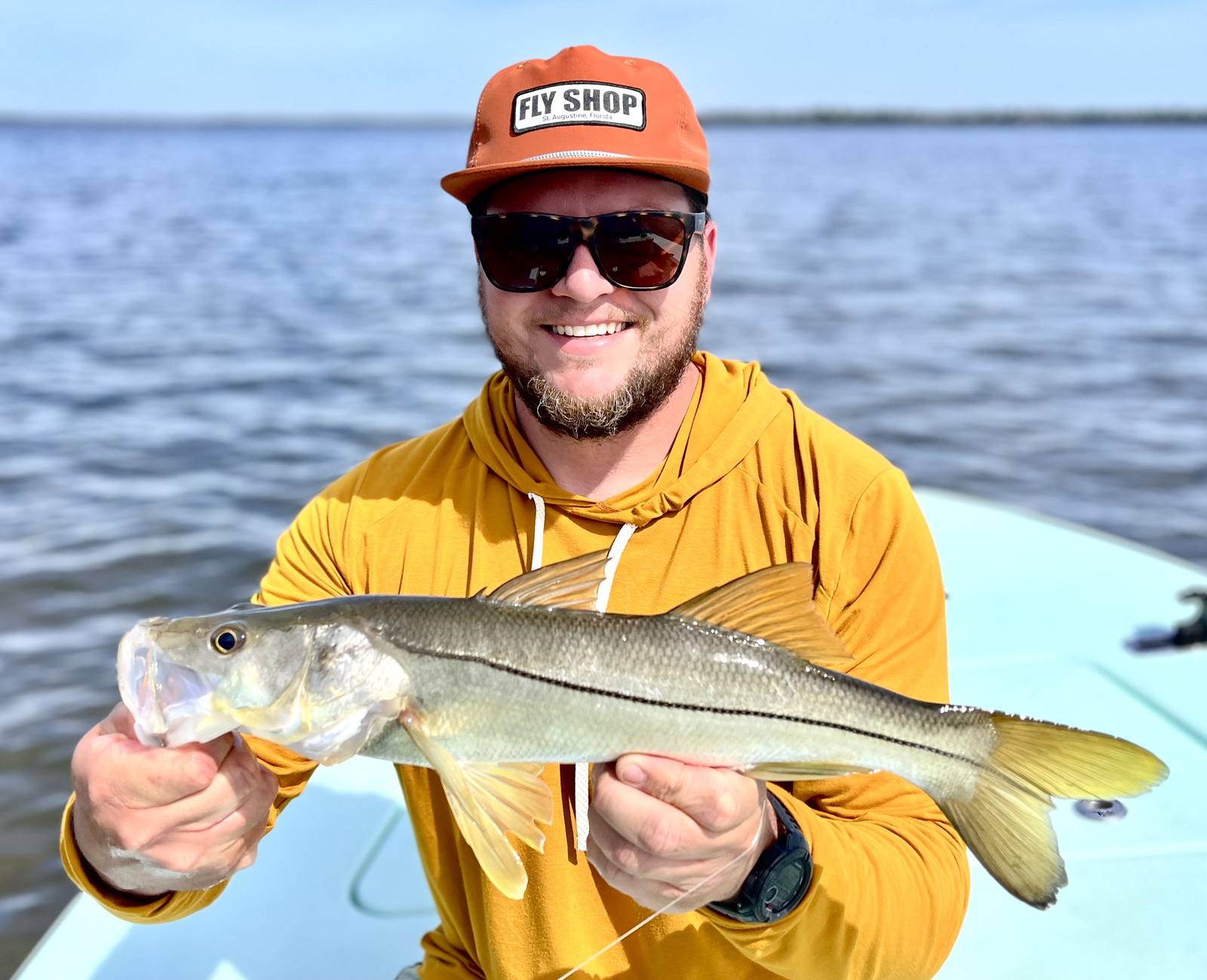 Angler in a yellow hoodie holding a snook